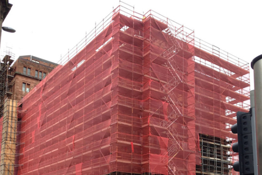 construction safety scaffolding protective bebris netting in red color surrounds the building